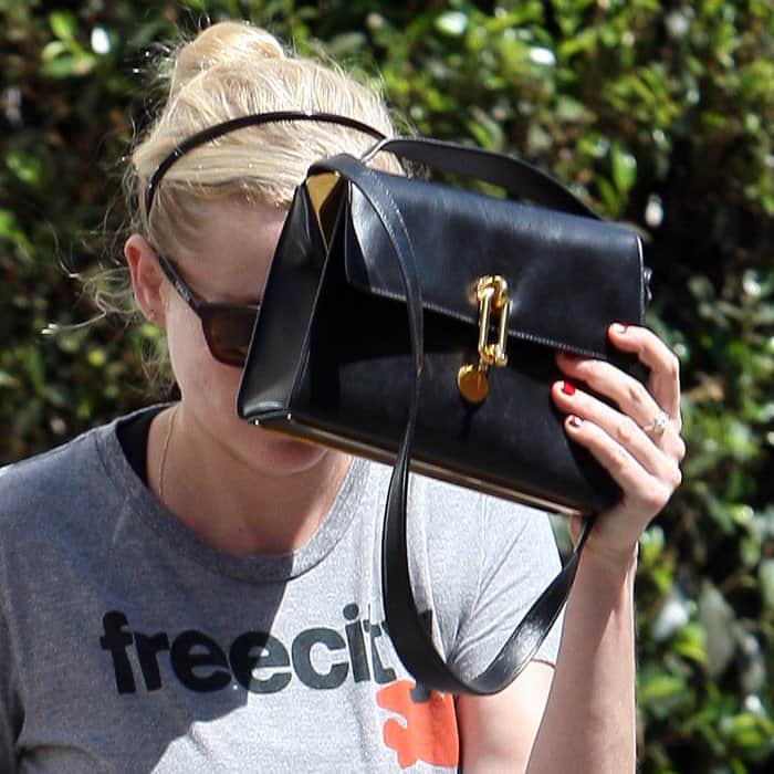 Kirsten Dunst showing off her boxy black crossbody that features a safety pin detail on its flap front