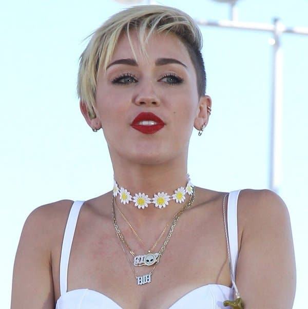 Miley Cyrus accessorizes with a sunflower choker and an Ok1984 X Kreayshawn Foreign Visitor necklace, adding a unique touch to her daring outfit