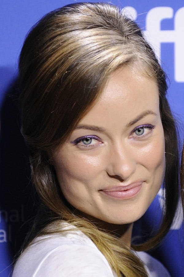 Olivia Wilde enchants with a subtle smile and striking blue eyes, highlighted by luminous skin and captivating purple eyeliner