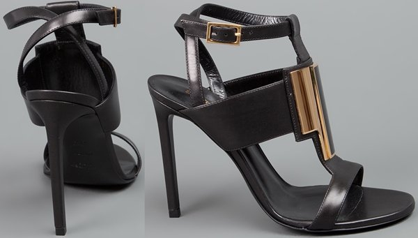 Black Saint Laurent "Janis" sandals with thick t-straps in front, a gold plaque detail, wrap-around ankle straps, and leather-covered stiletto heels