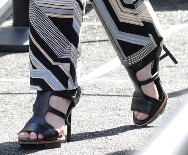 Coco Rocha steps out in striking black strappy sandals with architectural heels, perfectly complementing her bold patterned pants