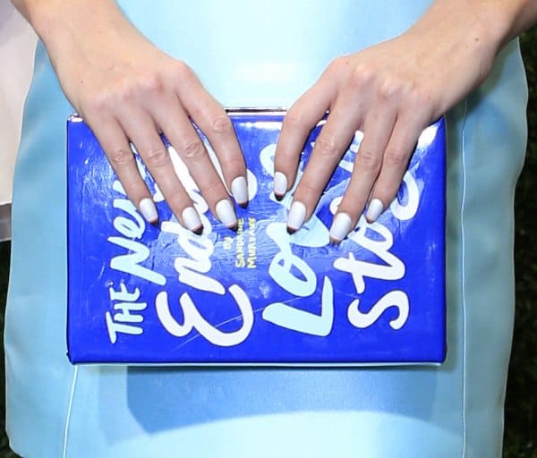 A detailed view of a vibrant blue 'The Never Ending Love Story' clutch, showcased by elegantly manicured hands with white nail polish, adding a chic touch to a soft blue ensemble