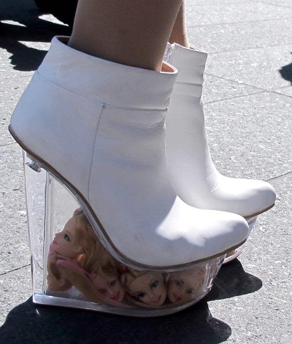 Unforgettable white wedge booties with a transparent heel filled with doll heads make a bold and edgy fashion statement