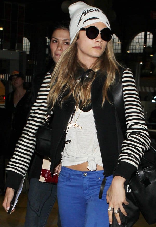 Cara Delevingne spotted in Paris on September 29, 2013, wearing a striped jacket, a knotted white tee, blue jeans, a beanie, and sunglasses, showcasing her casual chic style