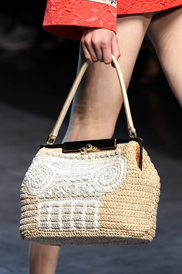 The intricate design and natural texture of the woven bag provide a perfect contrast to the bold, red ensemble, creating a stylish and sophisticated look
