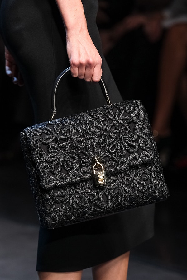 A timeless black handbag from Dolce & Gabbana's Spring/Summer 2014 collection, presented at Milan Fashion Week on September 22, features intricate embroidery and a gold clasp, adding a touch of elegance and sophistication to the classic black outfit
