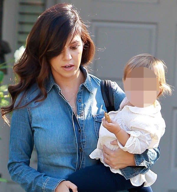Kourtney Kardashian rocks a double denim look, pairing a denim shirt with matching jeans, while carrying her child