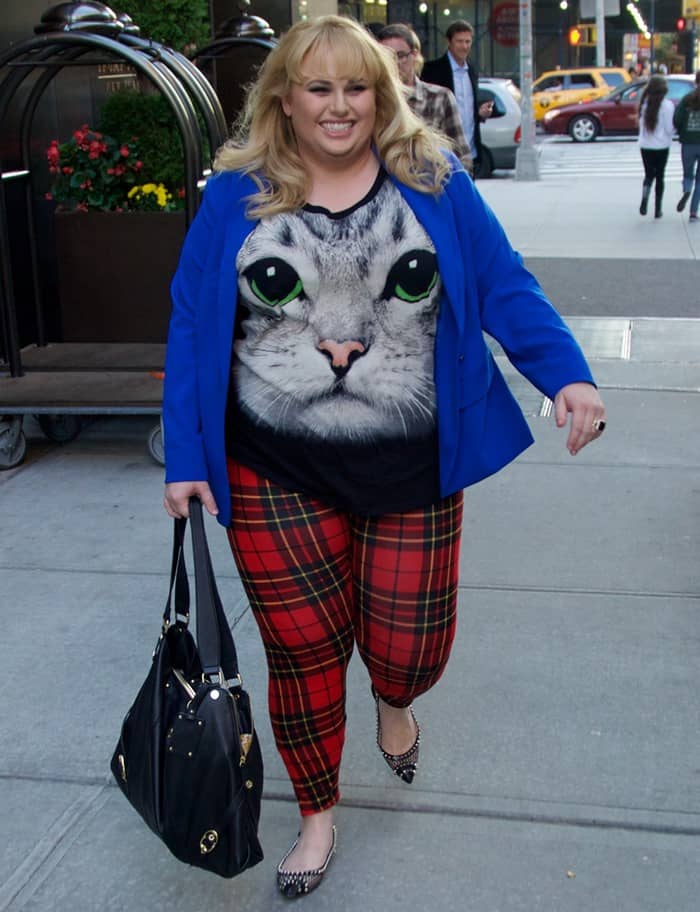 Rebel Wilson rocking a playful cat face print shirt with a bold cobalt blue blazer and red tartan leggings, adding a touch of whimsy and confidence to her vibrant street style