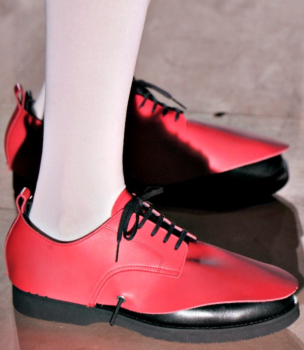 Vivid red oxford-style shoes with a bold black pointed overlay, blending classic structure with avant-garde detailing