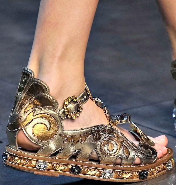 Gold Dolce & Gabbana flat sandals featuring intricate cut-out designs, jeweled embellishments, and ornate detailing around the sole embodying the brand's luxurious aesthetic