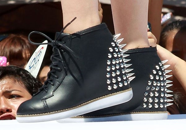 Cher Lloyd adds an edgy touch to her performance outfit with these black wedge sneakers, featuring bold silver spikes and studded detailing on the heels