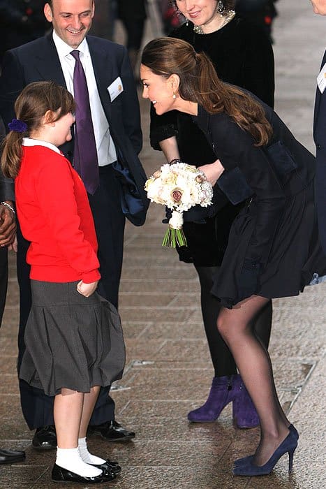 Kate Middleton talking with a school girl while taming a windblown skirt at the charity Place2Be in Canary Wharf in London, England on November 20, 2013