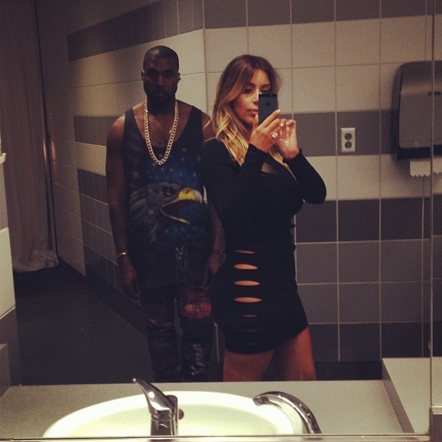 Kim Kardashian snaps a bathroom selfie in a cutout black dress, with Kanye West in the background, just before his Yeezus performance in Miami