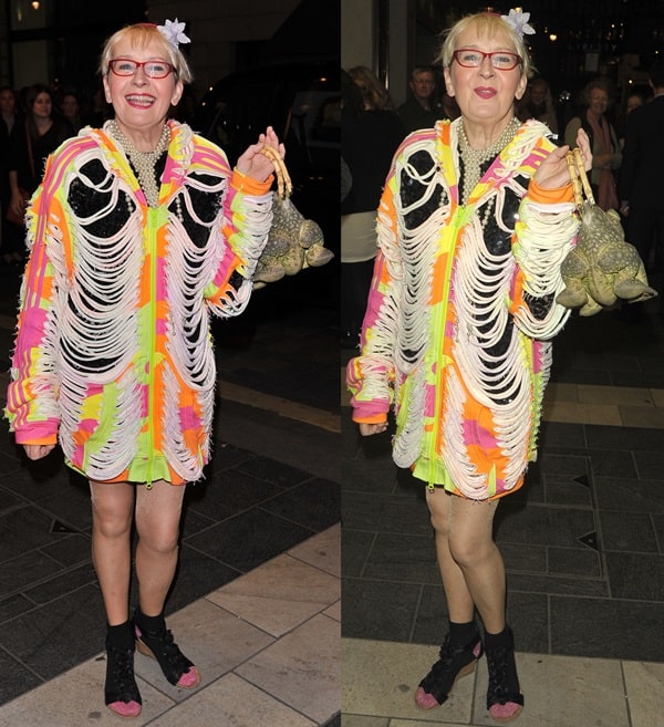 Su Pollard in a colorful, neon fringed jacket and black open-toe shoes, holding a frog-shaped purse at the 'Nutcracker on Ice' press night at the London Palladium