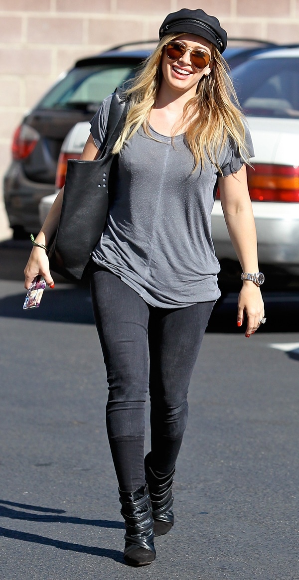 Hilary Duff beams with a bright smile, her loose, wavy blonde hair flowing under a trendy newsboy cap as she rocks her casual look with confidence