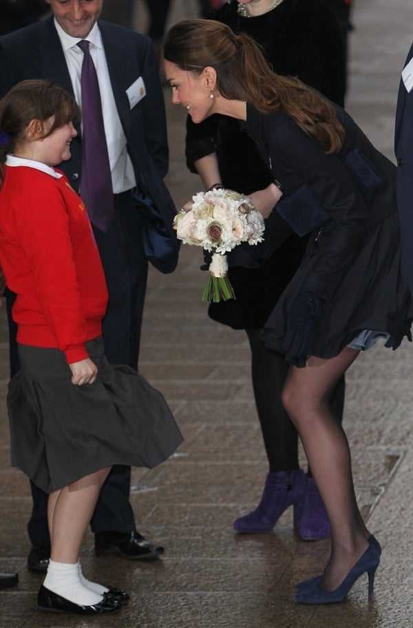 Kate Middleton trying to keep her skirt from getting blown by the wind as she receives a bouquet of flowers from a little girl at a Place2Be charity event in London on November 20, 2013