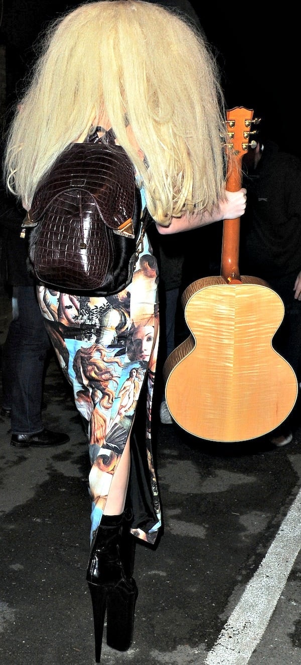 Lady Gaga wears her hair long and big as she holds a guitar and balances in a pair of enormous platform stilettos