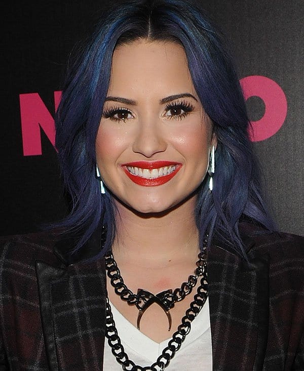 Demi Lovato stuns in a Marissa Webb plaid jacket, graphic tee, and bold statement jewelry, complemented by her vibrant blue hair and bright red lipstick