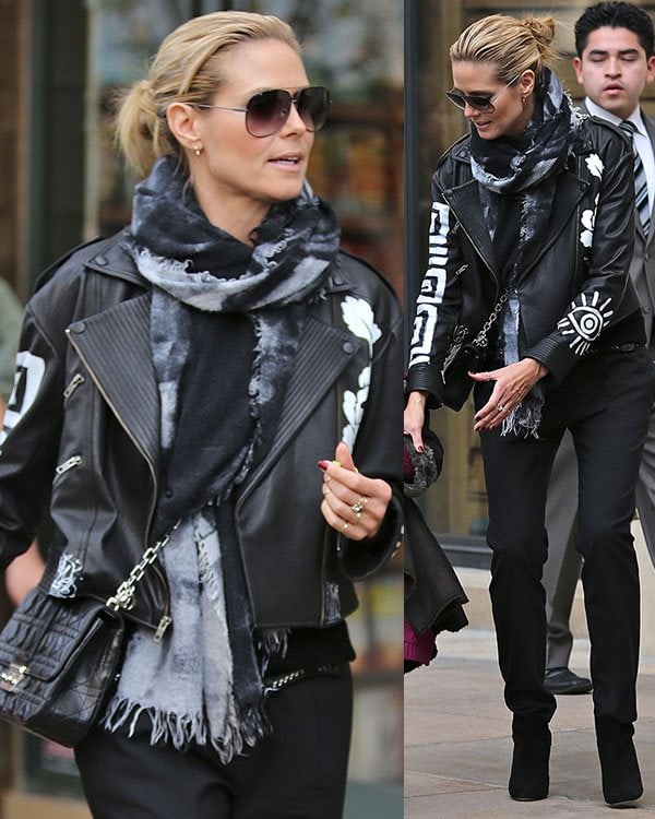 Heidi Klum wears a black Elizabeth and James Erwan leather moto jacket with a hand-painted design, triple zip welt pockets at the front, zip accents at the cuffs, black snap closures throughout, and exposed zip closure at front