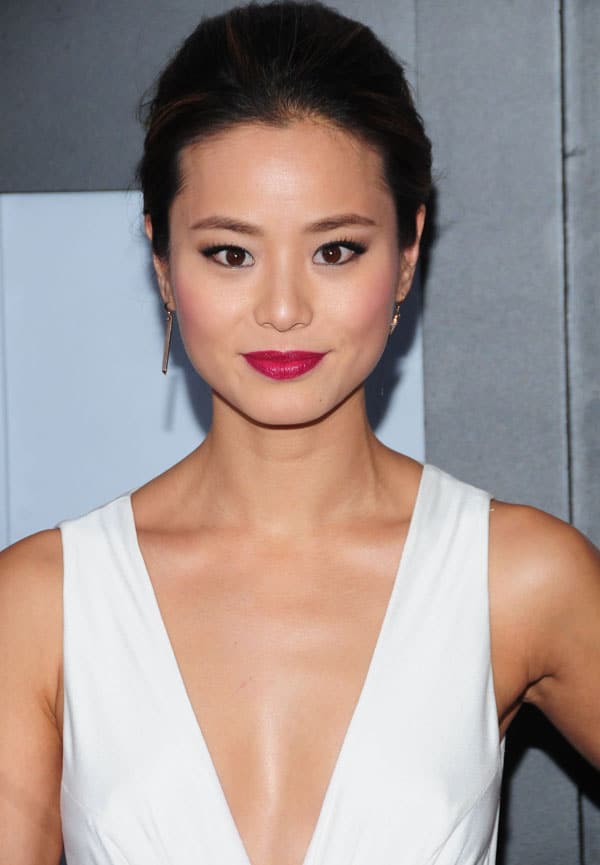 Jamie Chung with flawless makeup, featuring a bold lip color and striking eye makeup, wearing a white dress with a deep V-neckline