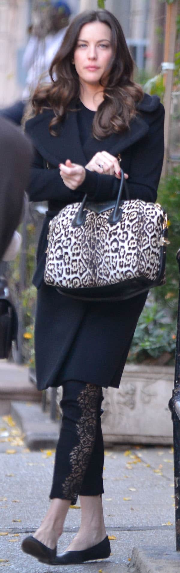 Liv Tyler wearing a black coat, lace-paneled leggings, leopard-print handbag, and flats while walking in New York City