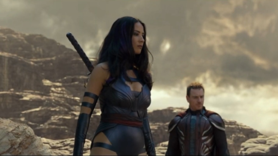 Olivia Munn as Psylocke in X-Men: Apocalypse, wearing her iconic purple and black latex costume, complete with a sword, standing alongside Michael Fassbender as Magneto in an intense desert setting