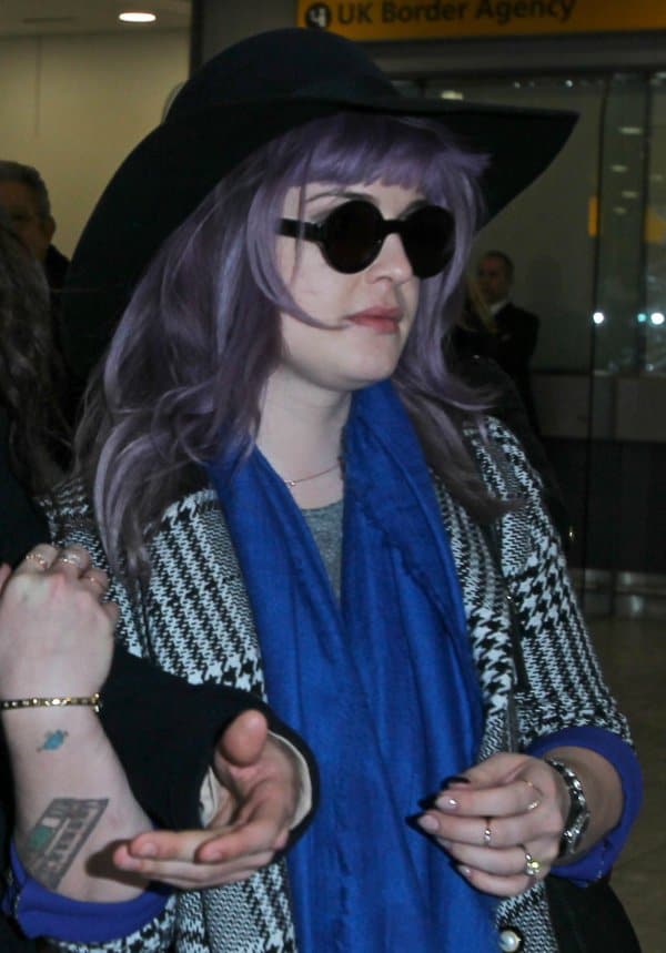 Kelly Osbourne stood out at Heathrow airport with her light purple hair, houndstooth coat, and bright blue scarf