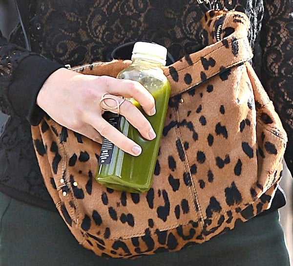 Mandy Moore accessorizes with a trendy leopard-print messenger bag, perfectly complementing her chic outfit while carrying a refreshing green juice