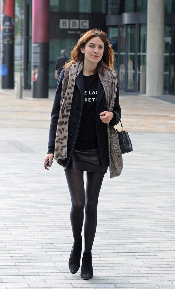 Alexa Chung layered a leopard print scarf over a black coat and leather skirt for a chic and edgy look