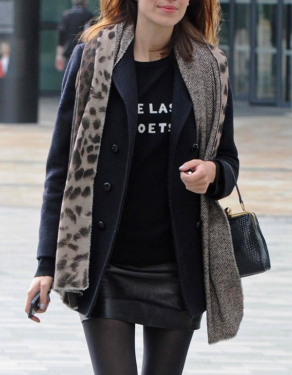 Alexa Chung layers a leopard print scarf over a black coat and graphic sweater for a stylish look