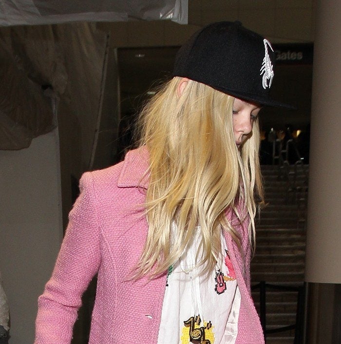 Elle Fanning covers her hair with a scorpion motif baseball cap at Los Angeles International Airport