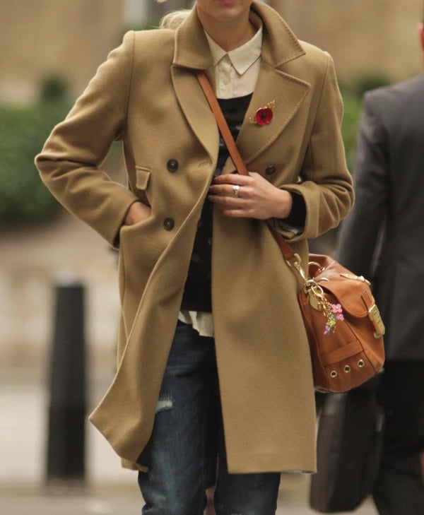 Fearne Cotton layers a camel trench coat over a collared shirt and sweater, accessorized with a brown leather handbag for a sophisticated look
