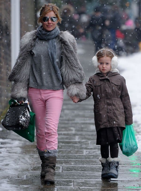 Geri Halliwell wearing pink skinny jeans, a gray fur coat, and boots while holding hands with her daughter Bluebell on a snowy day in London