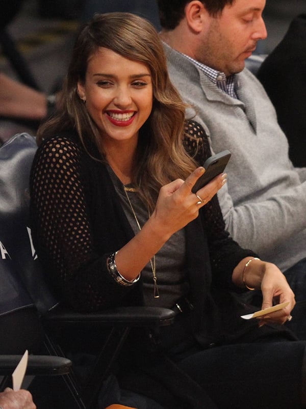 Jessica Alba enjoys the Lakers game courtside with a friend, looking stylish in a perforated cardigan and jeans