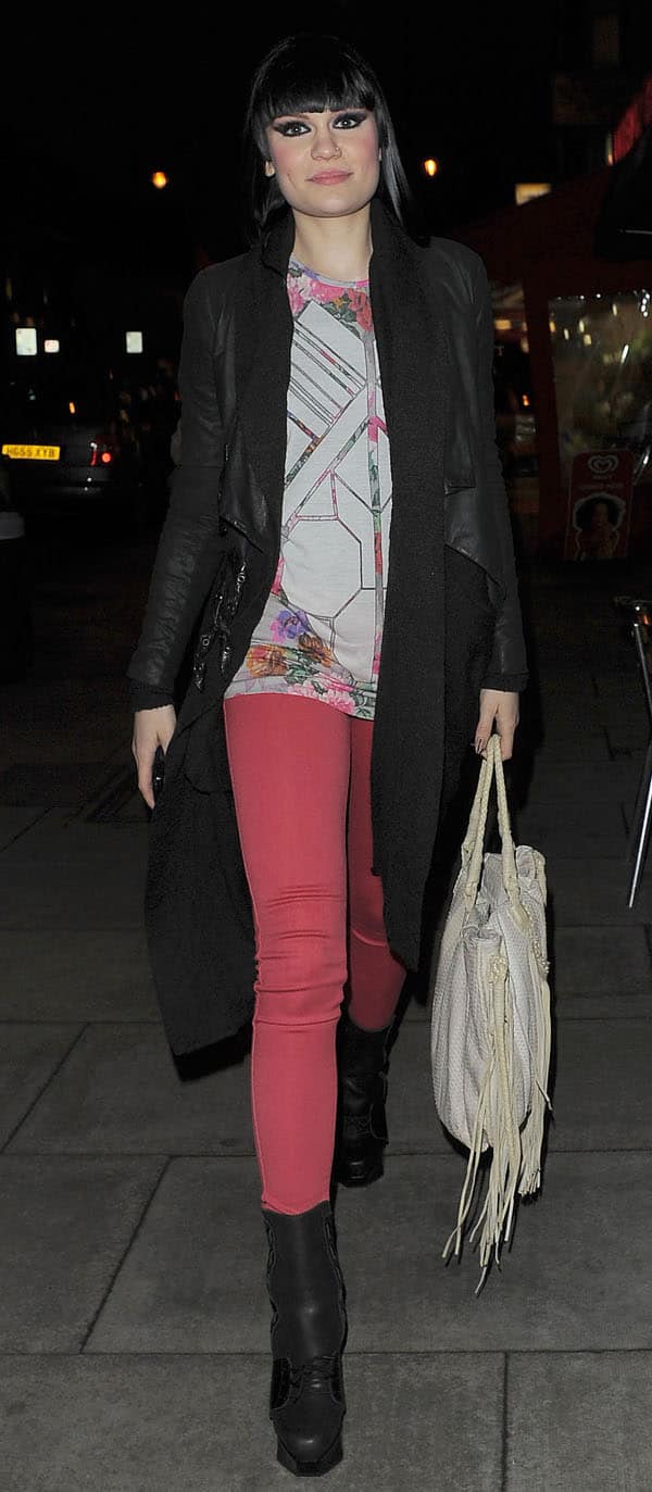 Jessie J wearing pink skinny jeans paired with a long black coat, a geometric print shirt, and platform boots while carrying a white fringed bag