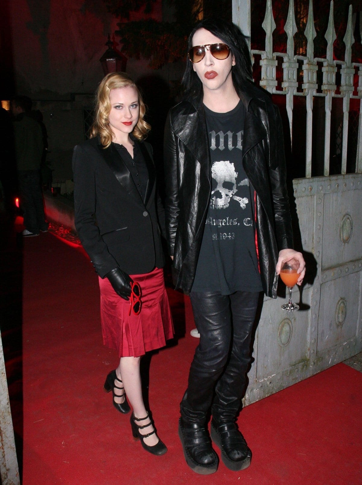 Marilyn Manson and girlfriend Evan Rachel Wood make a striking appearance at his Eat Me, Drink Me album listening session in Berlin on April 20, 2007, with Evan in a red satin pleated skirt, black satin-lapel blazer, and Mary Jane heels, while Manson opts for rocker-chic leather and towering platform boots
