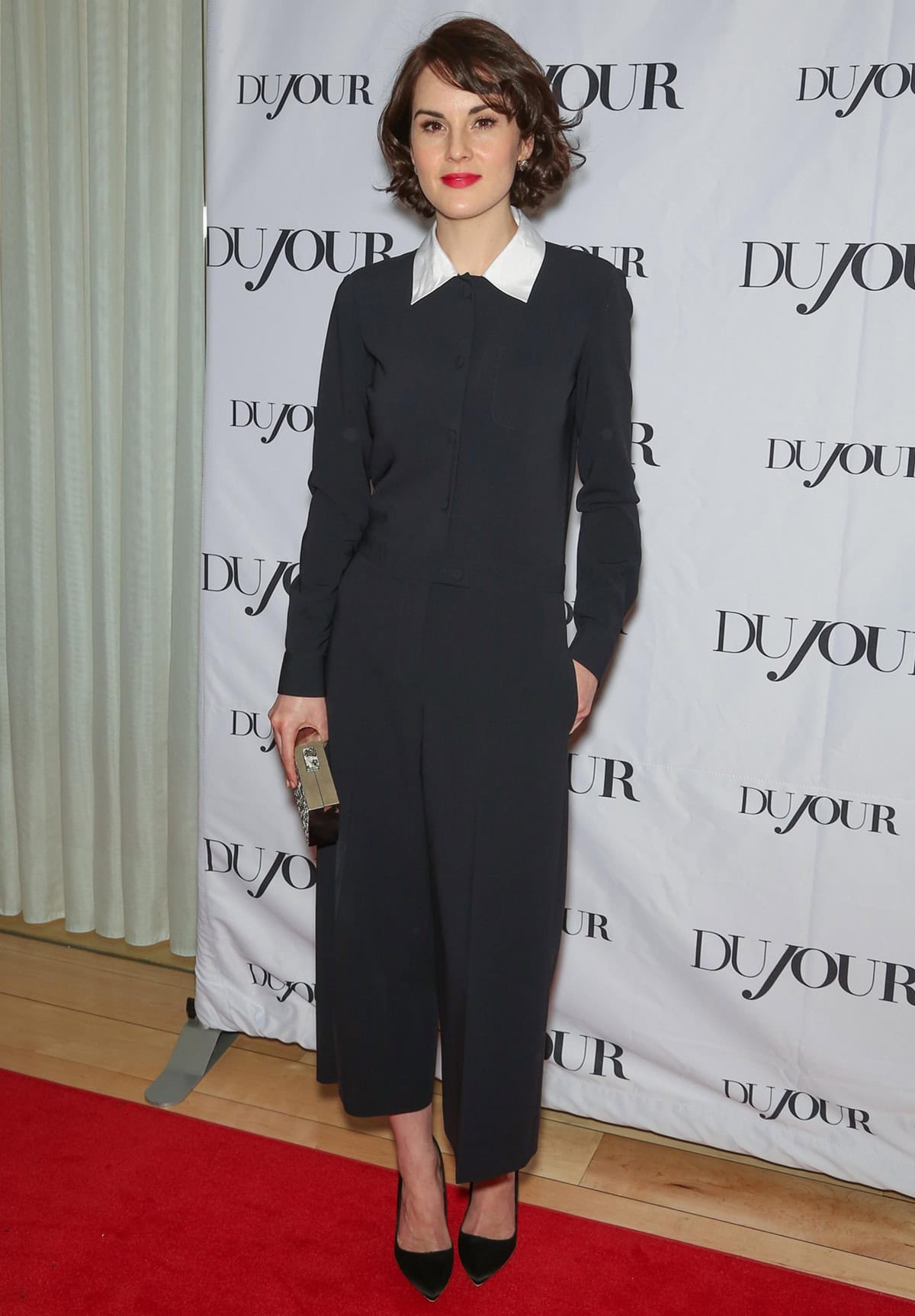 Michelle Dockery showcases a masterclass in minimalism with impact at DuJour magazine’s Great Performances issue celebration, pairing a Moschino jumpsuit with a playful Peter Pan collar and timeless Rupert Sanderson “Elba” pumps