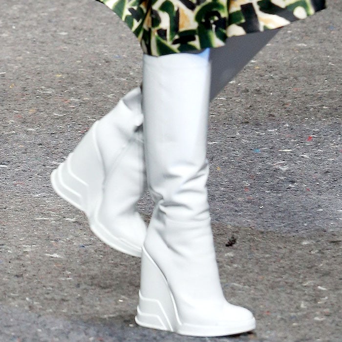 Prada's striking knee-high wedge boots in pristine white, featuring a seamless sculptural design, combine futuristic aesthetics with bold functionality