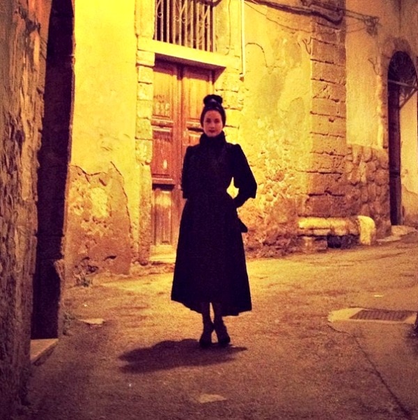 Dita Von Teese roams the dimly lit streets of Sicily in an elegant all-black ensemble, exuding her signature retro glamour