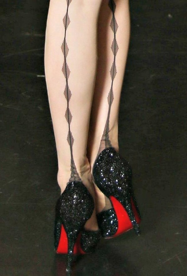 Dita Von Teese's dazzling black Louboutin heels with iconic red soles perfectly complement her sheer stockings, adorned with striking back-seam detailing for an added touch of vintage glamour