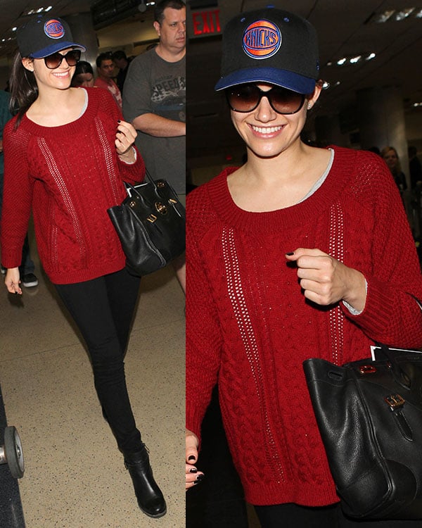Emmy Rossum at LAX Airport on March 16, 2014, wearing a New York Knicks cap and sunglasses, smiling as she pairs a Lovers + Friends so good sweater with black jeans and a Ralph Lauren Ricky bag