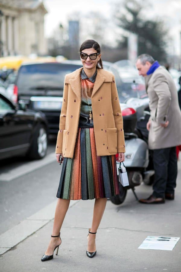 Giovanna Battaglia dazzles in a gradient top and pleated rainbow skirt, perfectly balanced with a chic camel coat and stylish ankle-strapped heels