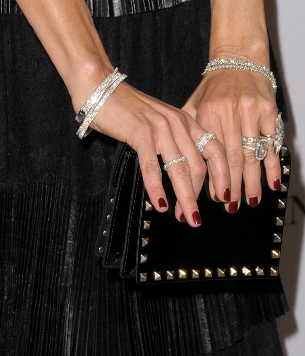 Rachel Zoe's hands adorned with sparkly diamond rings and bracelets, holding a chic studded clutch, perfectly complement her vintage-glam Valentino dress
