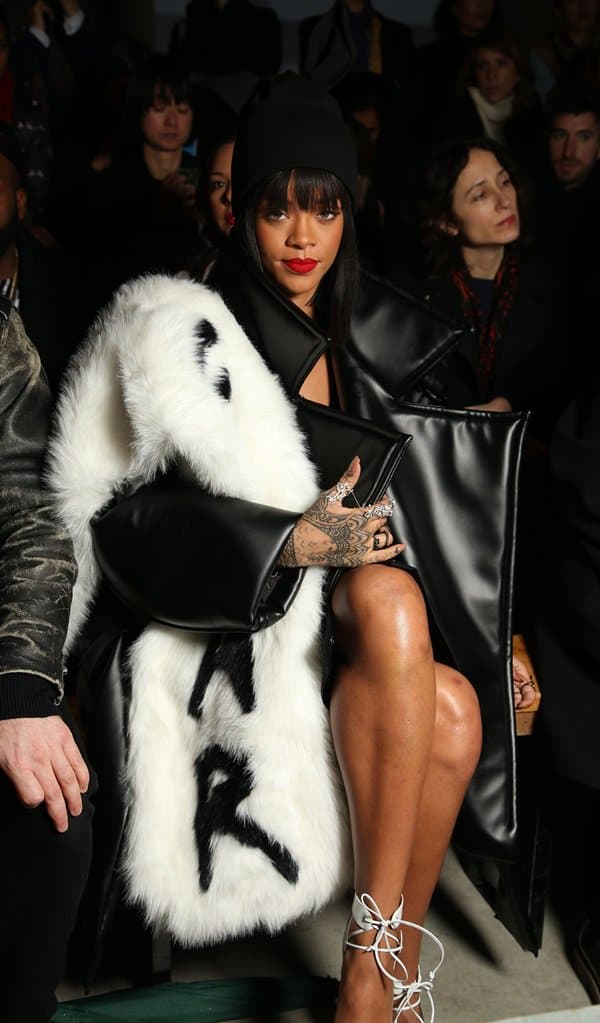 Rihanna attended the Comme des Garçons fashion show on March 1, 2014, wearing Manolo Blahnik Lara pumps, an Adam Selman Fall 2014 hat, a Vfiles Fall 2014 fear stole and coat, and Elise Dray white gold and grey diamond double ring along with a black gold and black diamonds mitaine spider web four finger ring.
