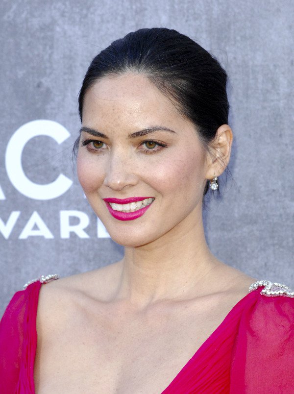 Olivia Munn radiates elegance with her sleek updo, vibrant pink lipstick, and delicate diamond drop earrings