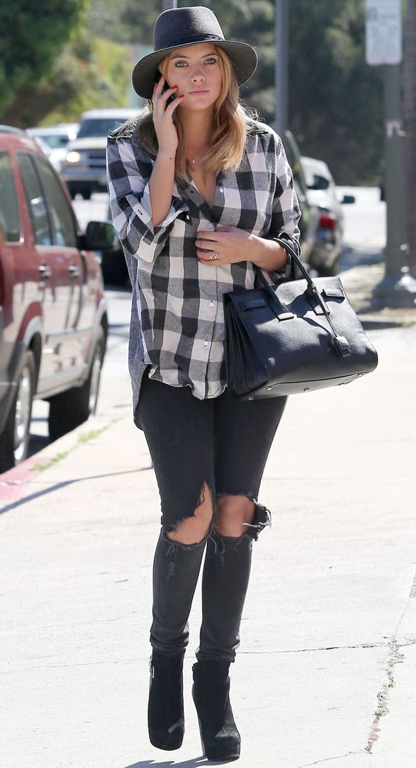 Ashley Benson adds a Western touch to her look with ripped knee jeans, an oversized plaid shirt, fedora, and suede boots, balanced by a structured black tote for a hint of city style
