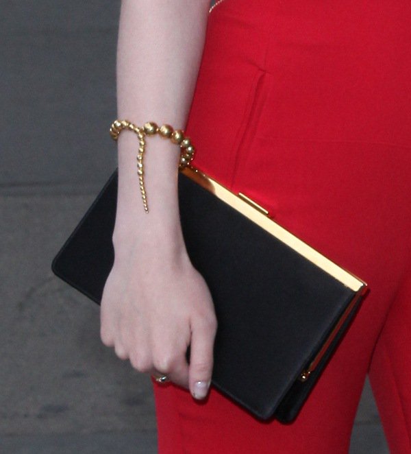 Dakota Fanning pairs her sleek black clutch with elegant gold bracelets, perfectly complementing her red jumpsuit