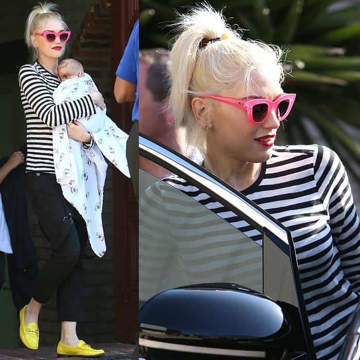Gwen Stefani cradles baby Apollo while showcasing her chic Memorial Day look with a striped tee, black overalls, pink cat-eye sunglasses, and vibrant yellow loafers