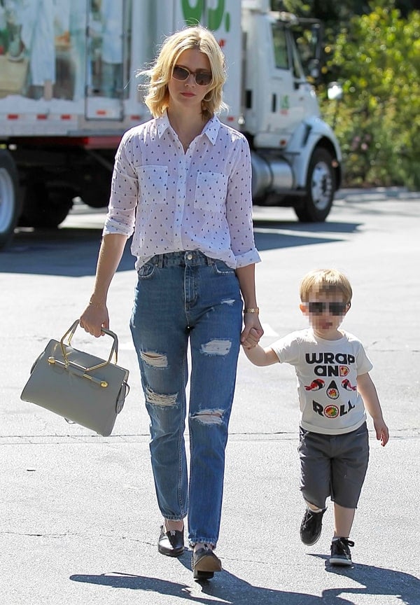 January Jones brings a retro flair to her daytime attire, tucking a button-down shirt into high-waisted distressed jeans, completed with loafers and a satchel bag for a classic, chic look