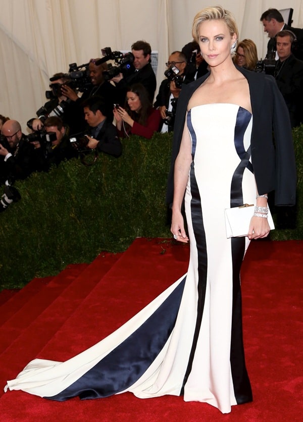 Charlize Theron stuns in a black-and-white Dior Couture gown with a dramatic train, completing her look with a structured black jacket and a white satin Dior clutch